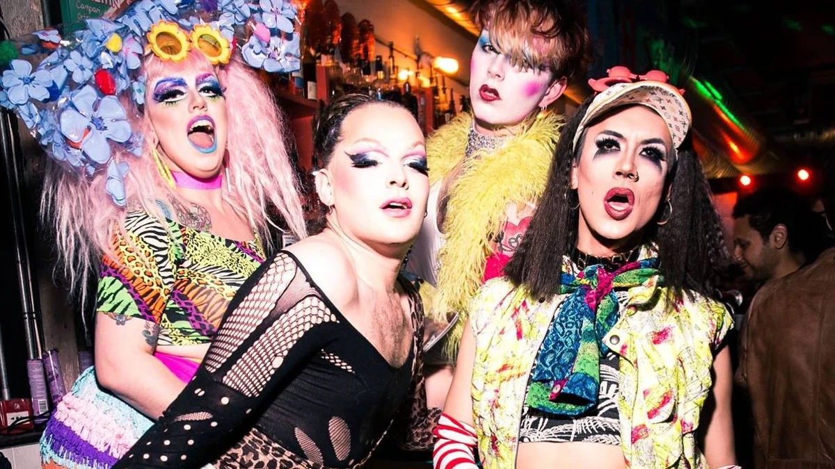 Four performers in bright drag posing together at the bar in a London queer venue